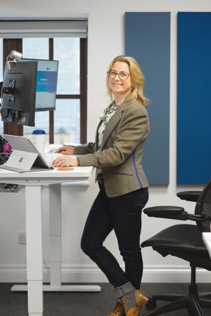 Professional working at a modern standing desk setup with dual monitors in a bright office space with blue accent walls.
