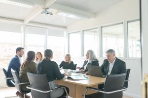 Business professionals meeting around a conference table in a bright modern office with glass windows.