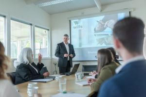 Business professionals attending a presentation in a bright conference room with projector screen.