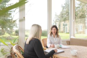Two professionals having a business meeting on a sunny enclosed porch with paperwork and coffee cups on the table.
