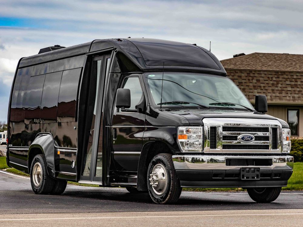 Black Ford luxury shuttle bus with custom exterior parked outside a brick building.