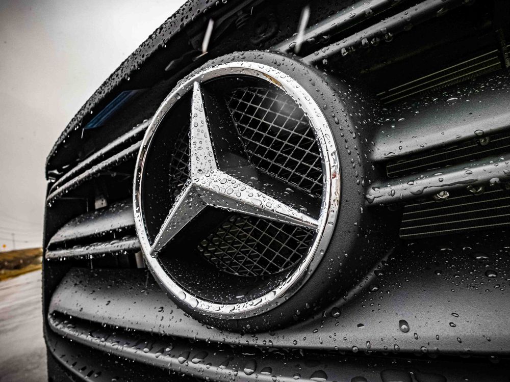 Mercedes-Benz emblem on black grille with raindrops in detailed macro shot.