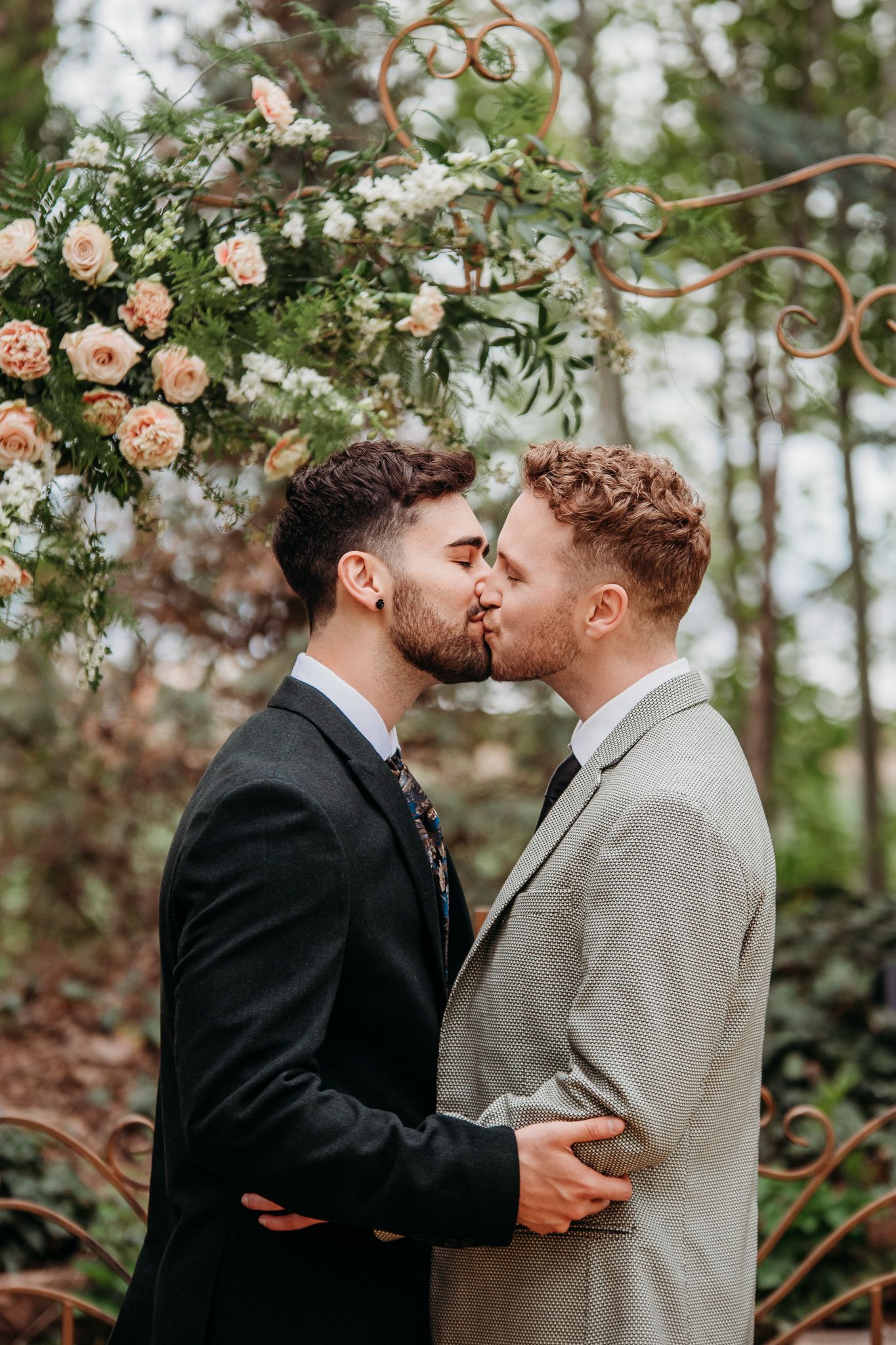 Romantic moment between two people under a floral archway in suits.