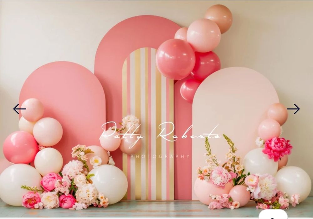 Pink and white balloon arch with floral decorations and striped backdrop for a baby shower or party.