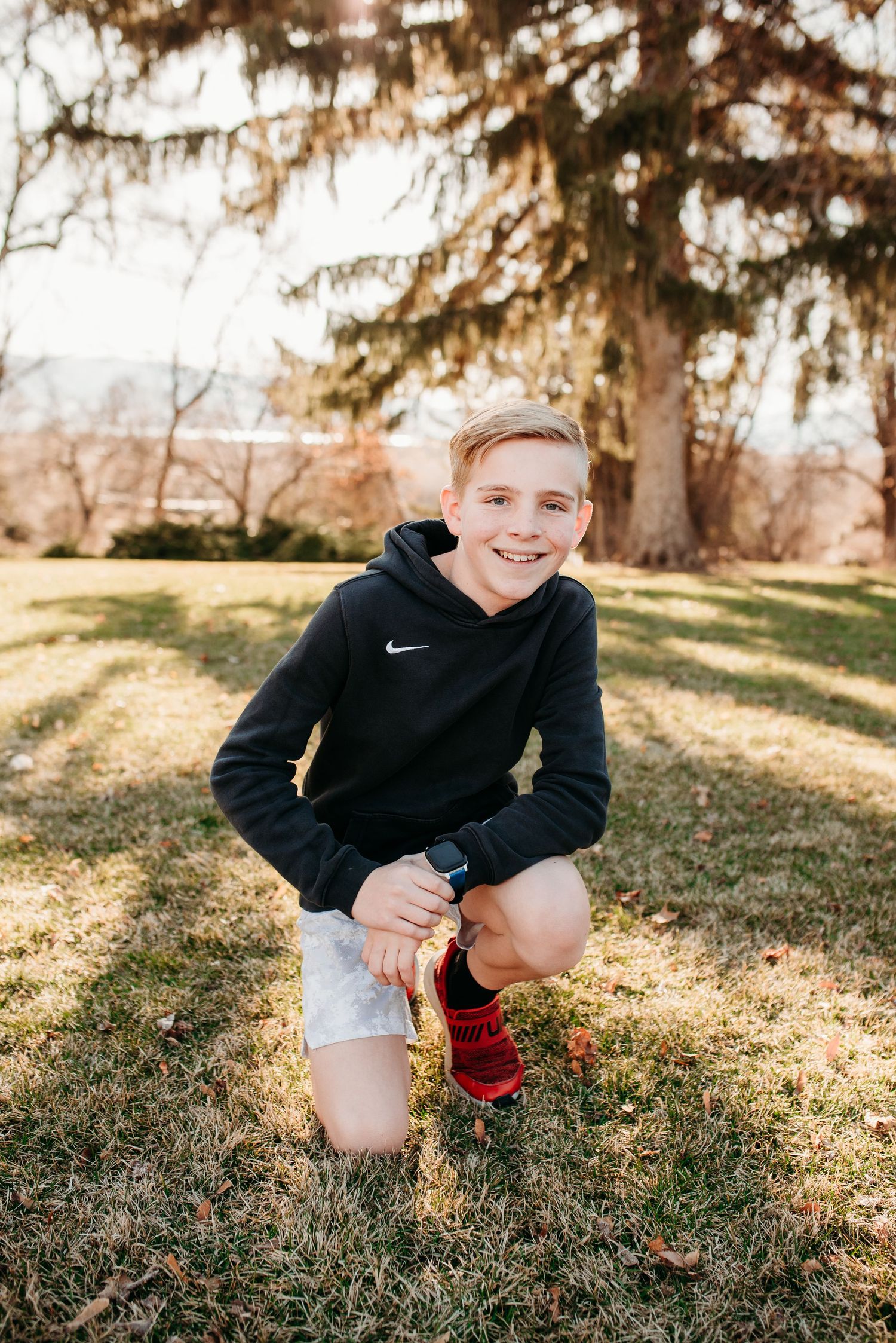 Person in Nike hoodie kneeling on grass with mismatched socks during outdoor photoshoot.