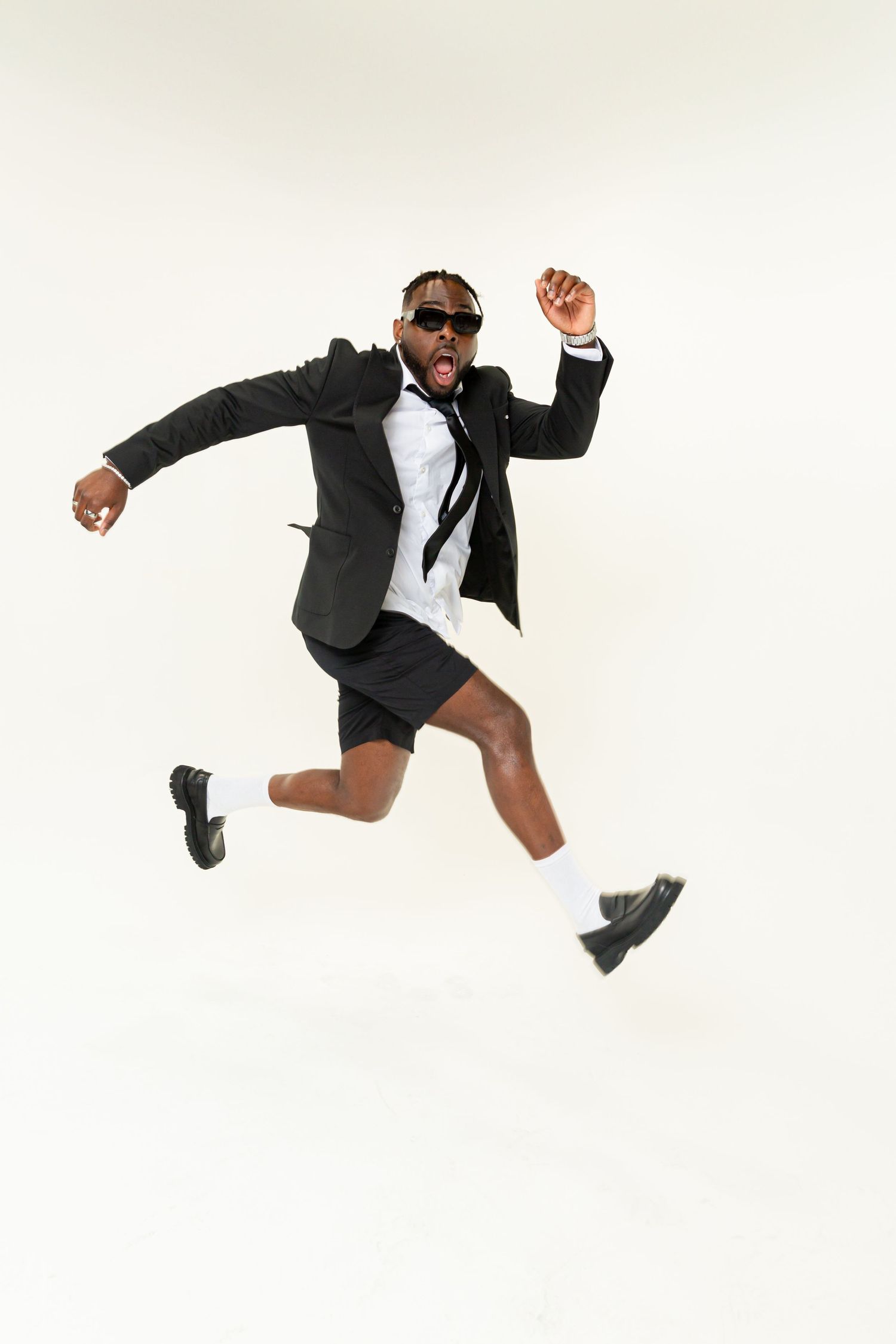 Business professional in a black suit and sunglasses leaps energetically against a white background.
