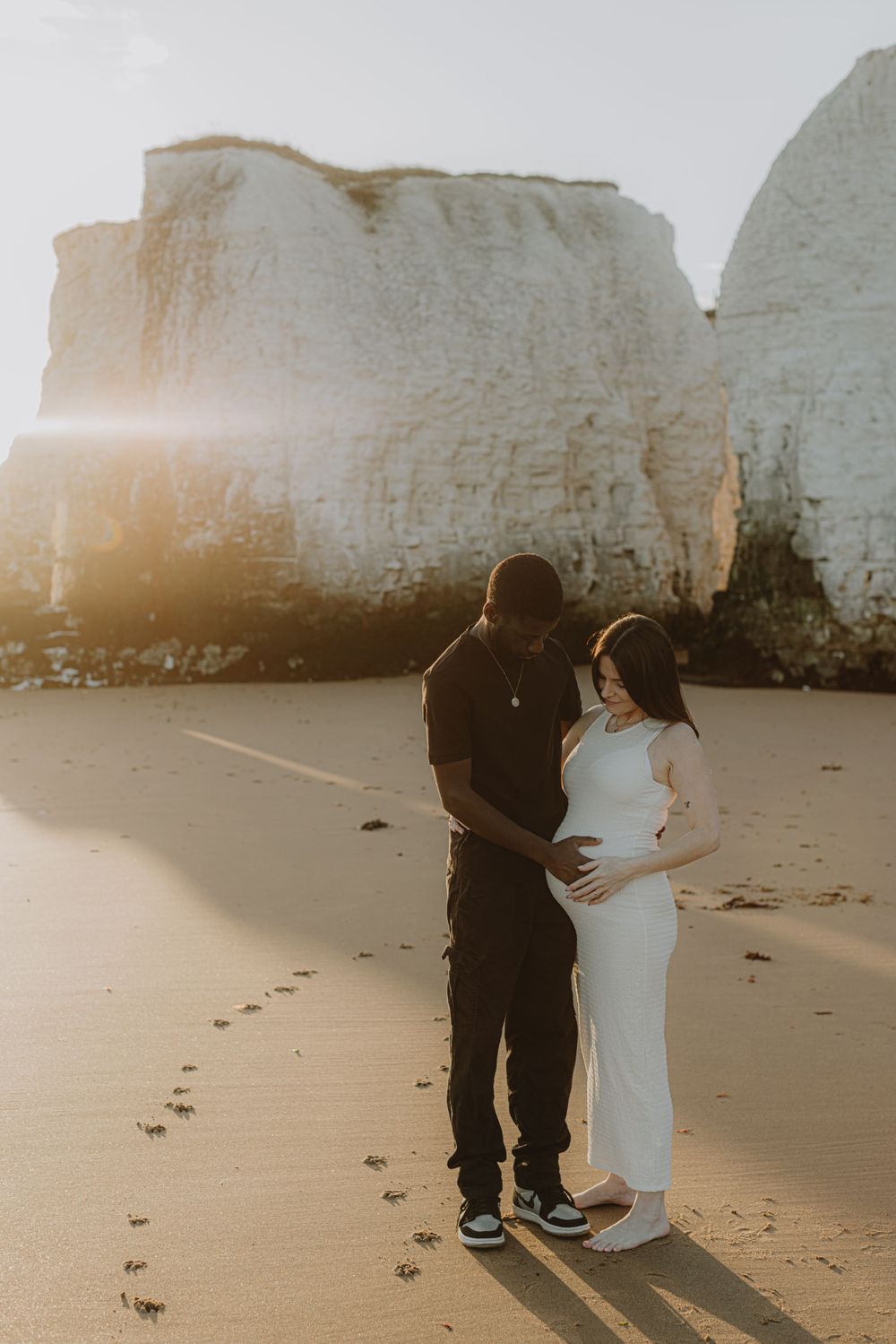 Maternity photo of couple on beach with dramatic white cliffs at sunset.