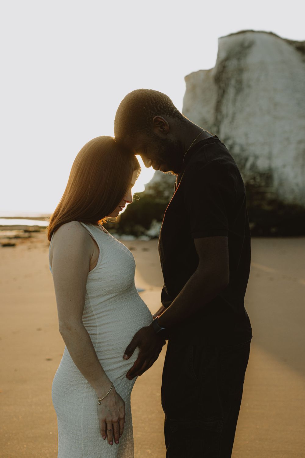 Intimate sunset maternity portrait on beach with white cliffs in background.