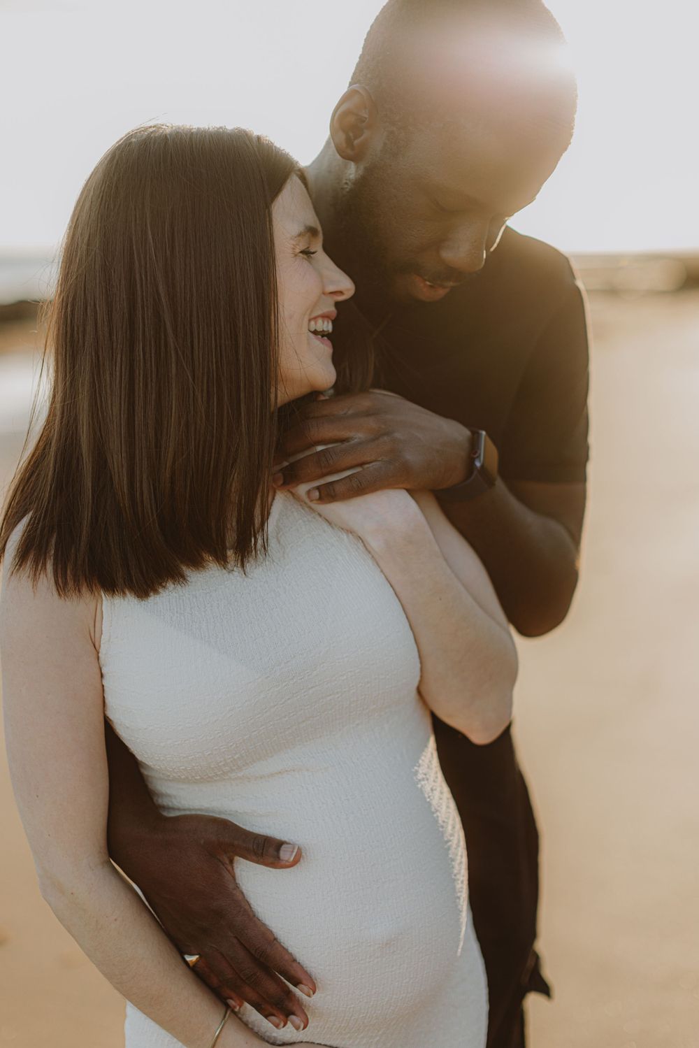 Intimate maternity photoshoot on the beach at sunset showing couple embracing.