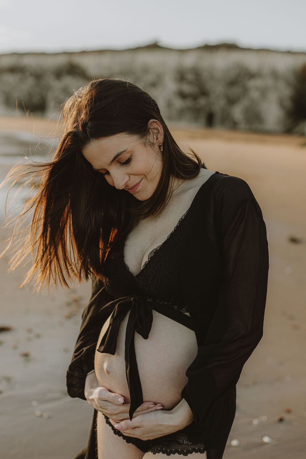 Maternity photography session with flowing black dress against warm sunlight.