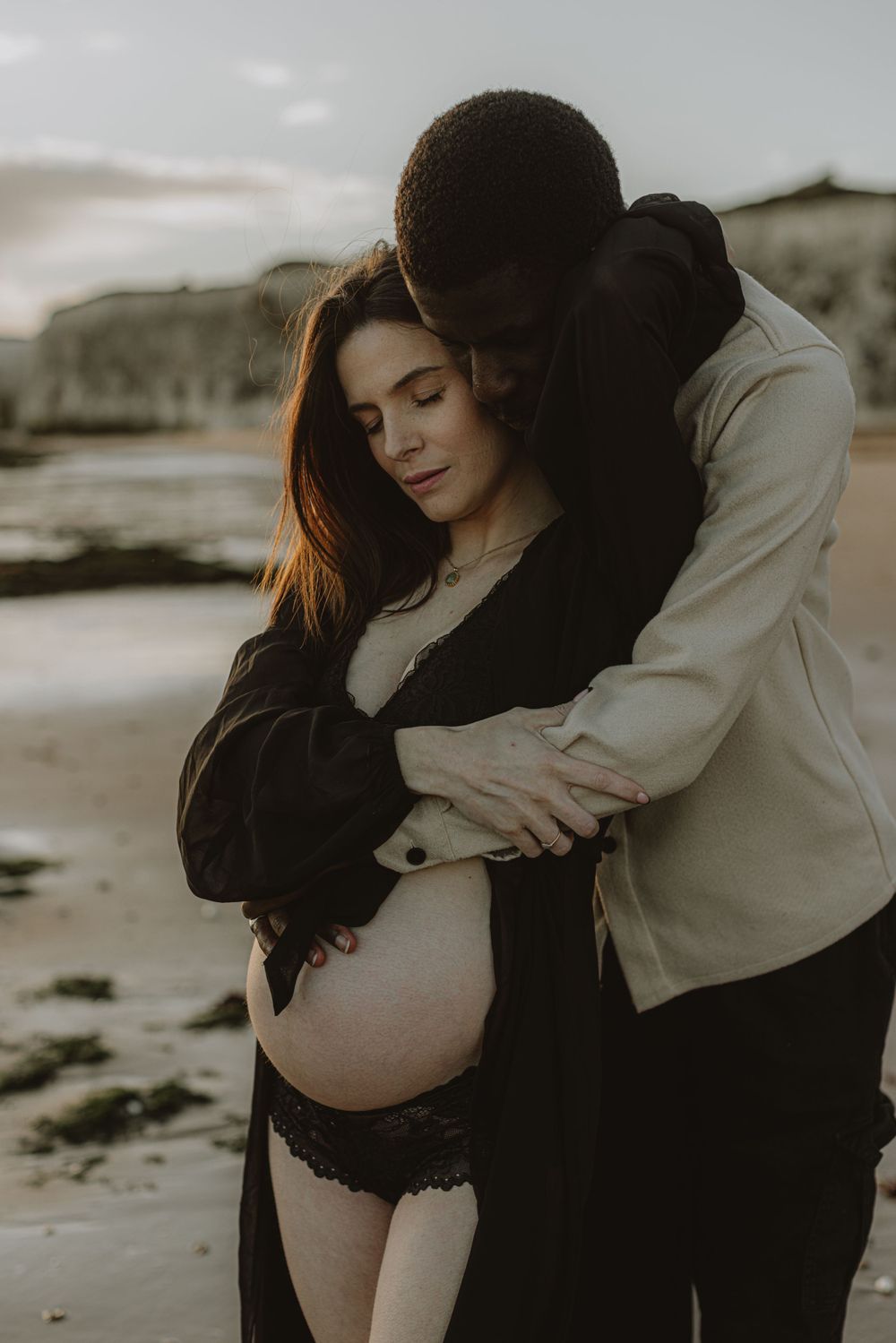 Artistic black and white maternity photos on rocky beach showing tender moments.