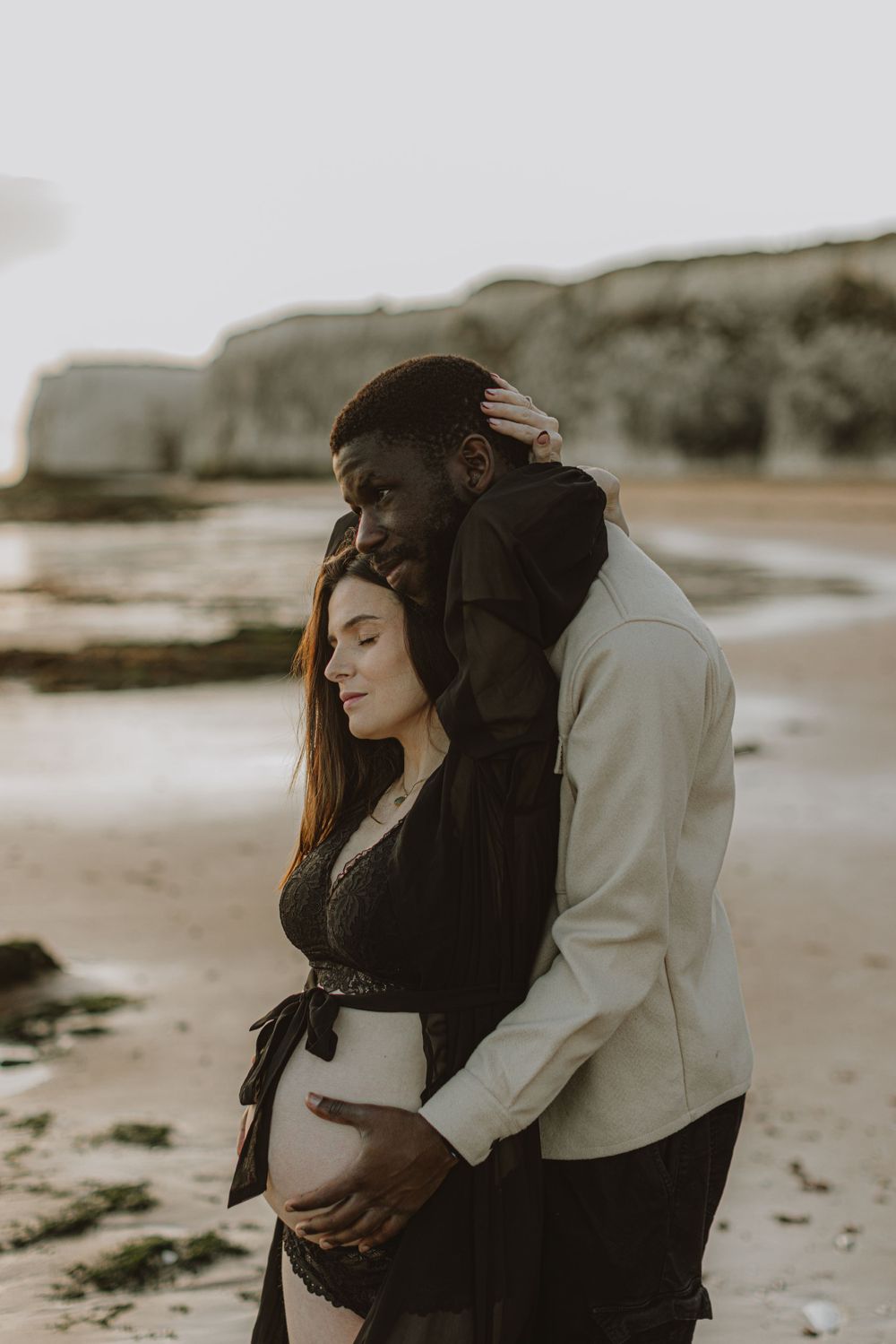 Moody beach maternity session captures intimate moments between couple.