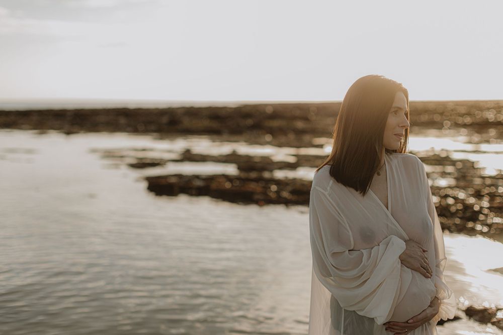 Sunset beach maternity session with couple in soft natural light.