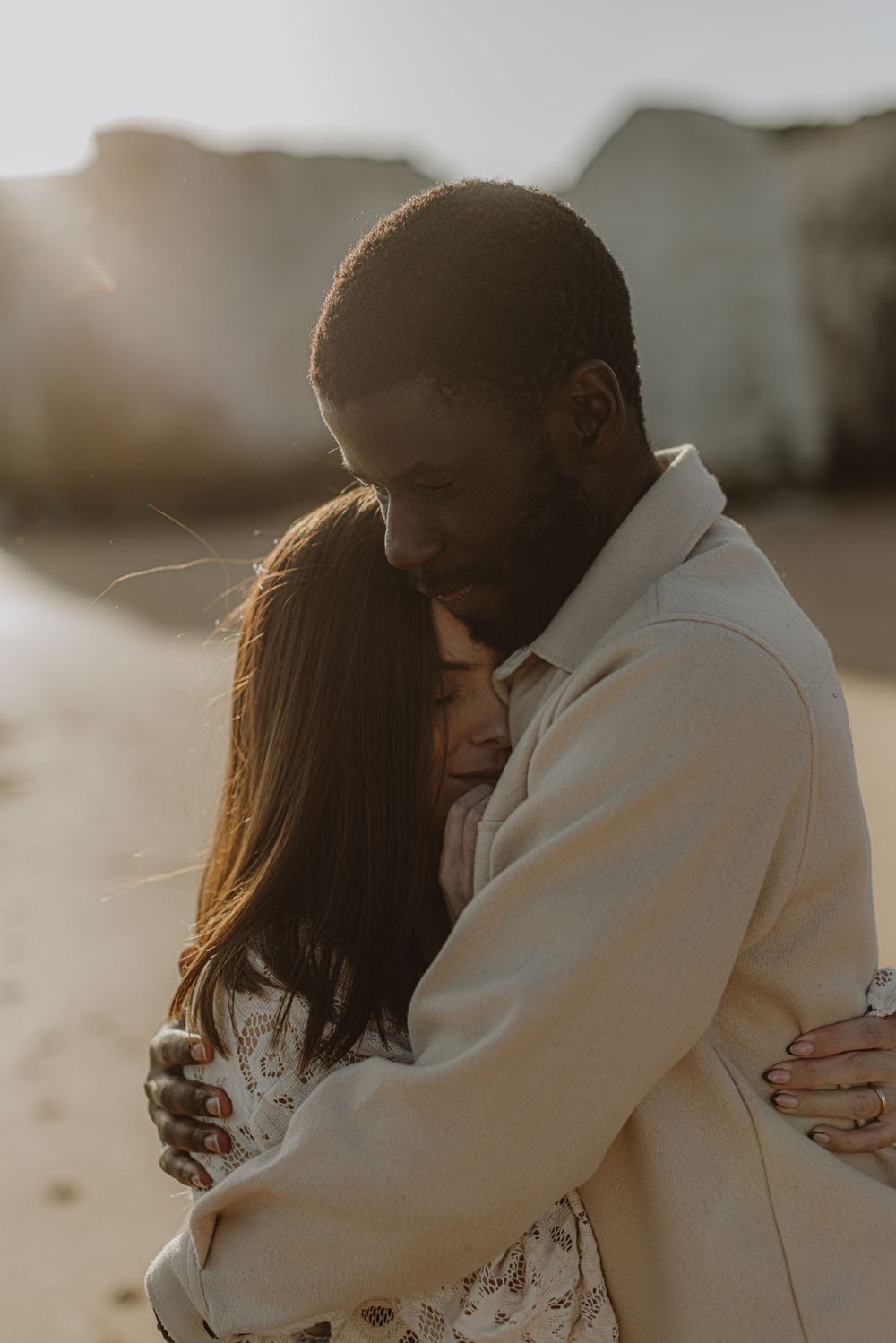A tender embrace between two people wearing white against a soft sunlit background.