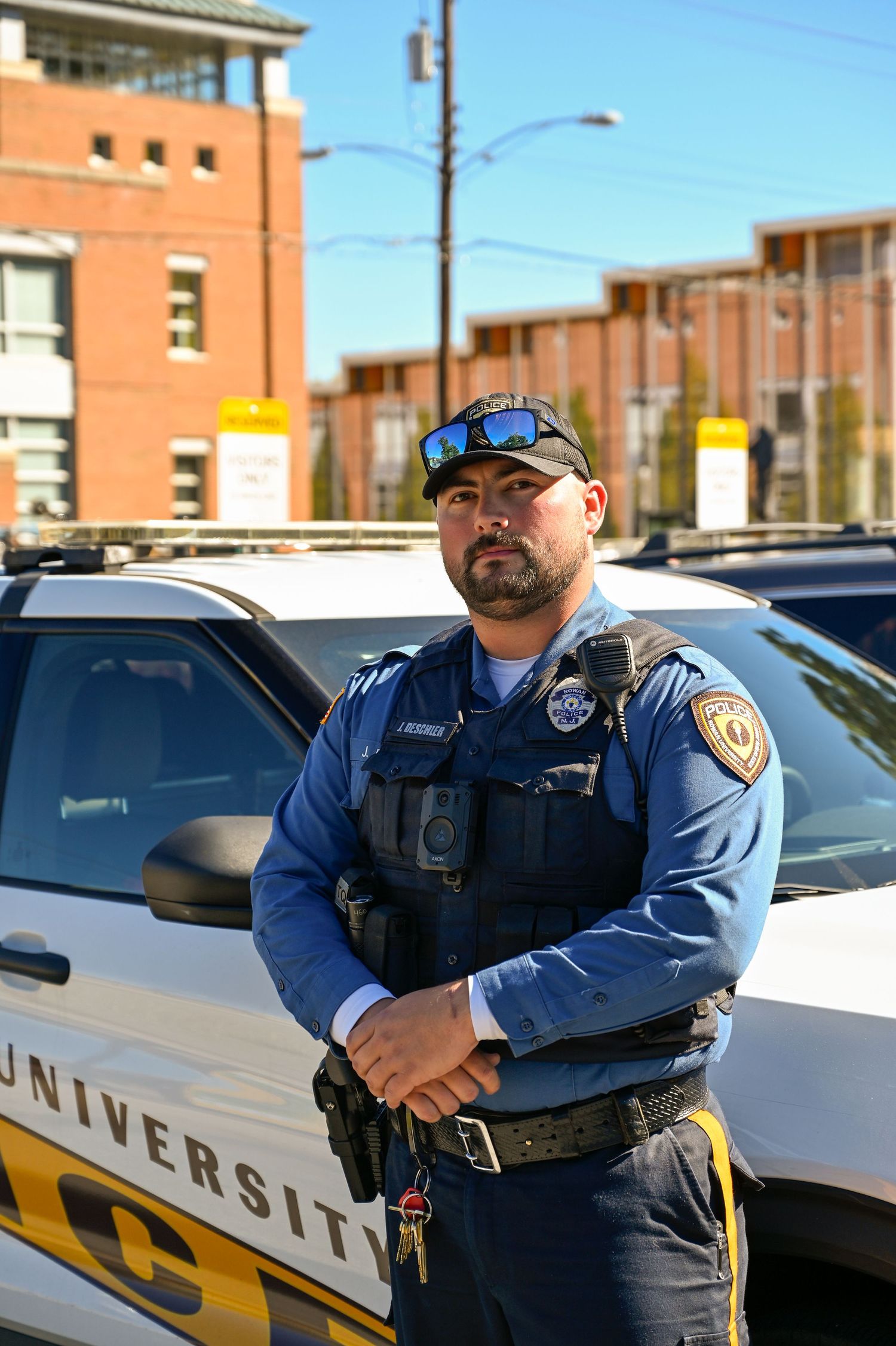 Campus security officer in uniform standing next to a university police vehicle.