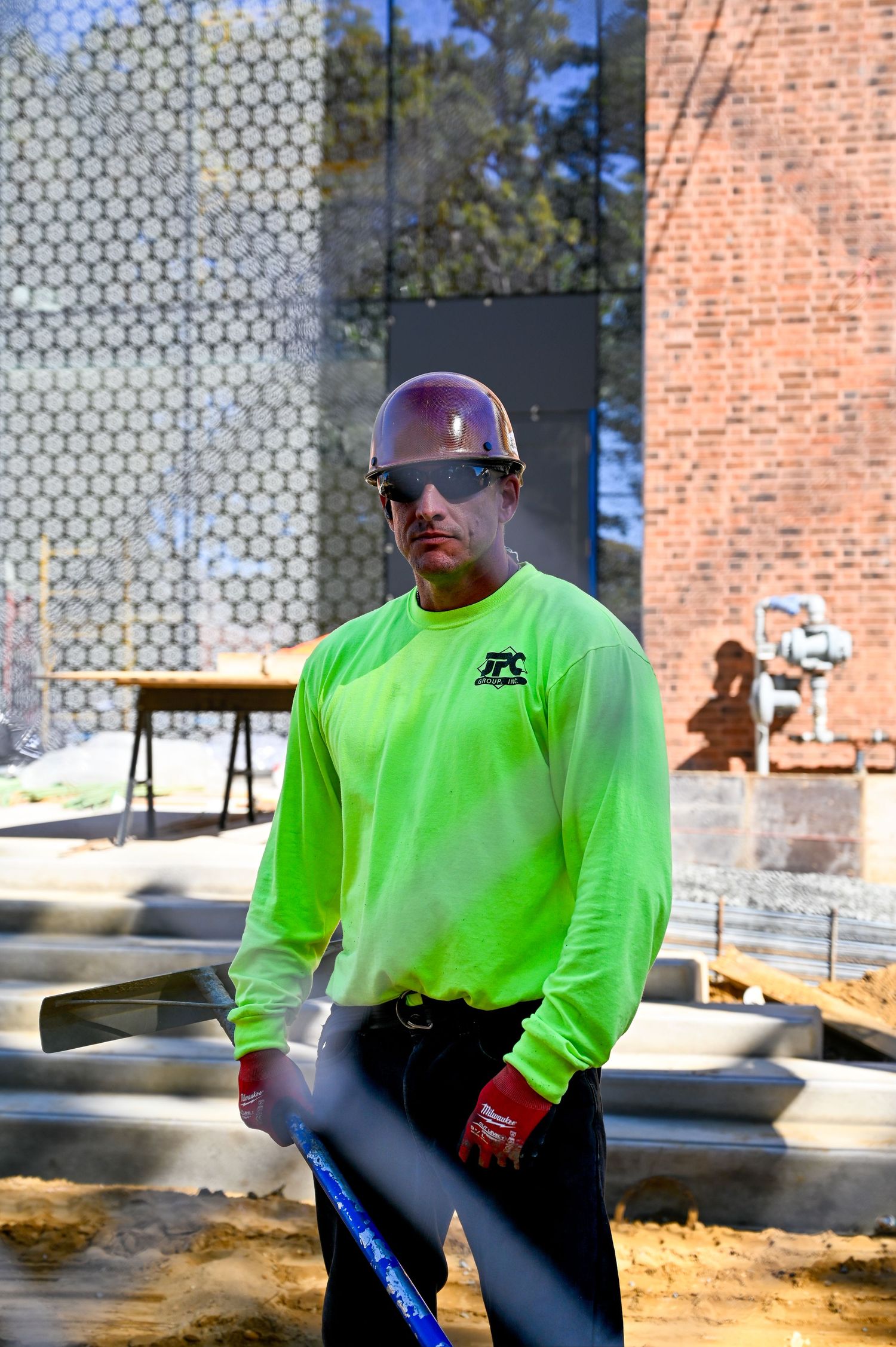 Construction worker in safety gear and bright green shirt at a building site.