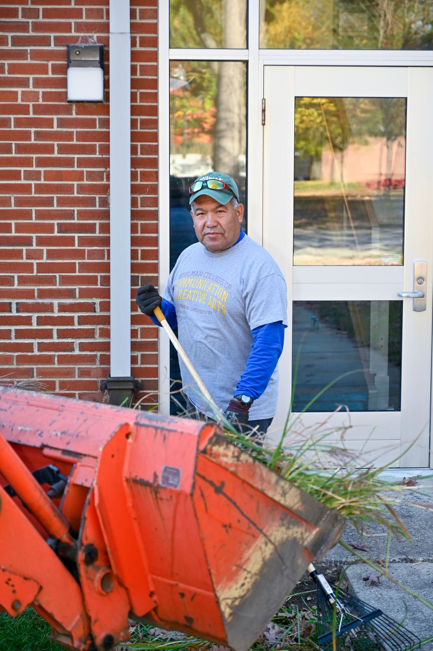 Orange tractor scoop visible near a brick building entrance with reflective glass windows.