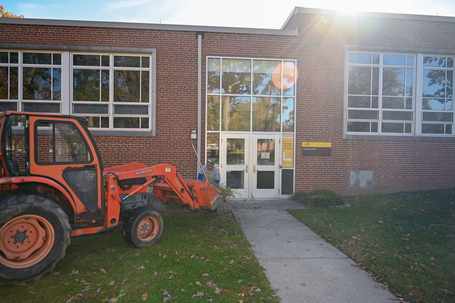 Orange tractor parked outside a brick school building entrance on an autumn day.