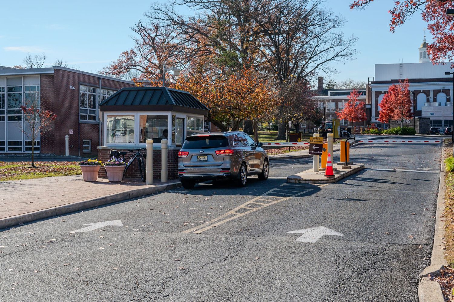 Campus entrance gate with security booth and traffic cones on an autumn day.