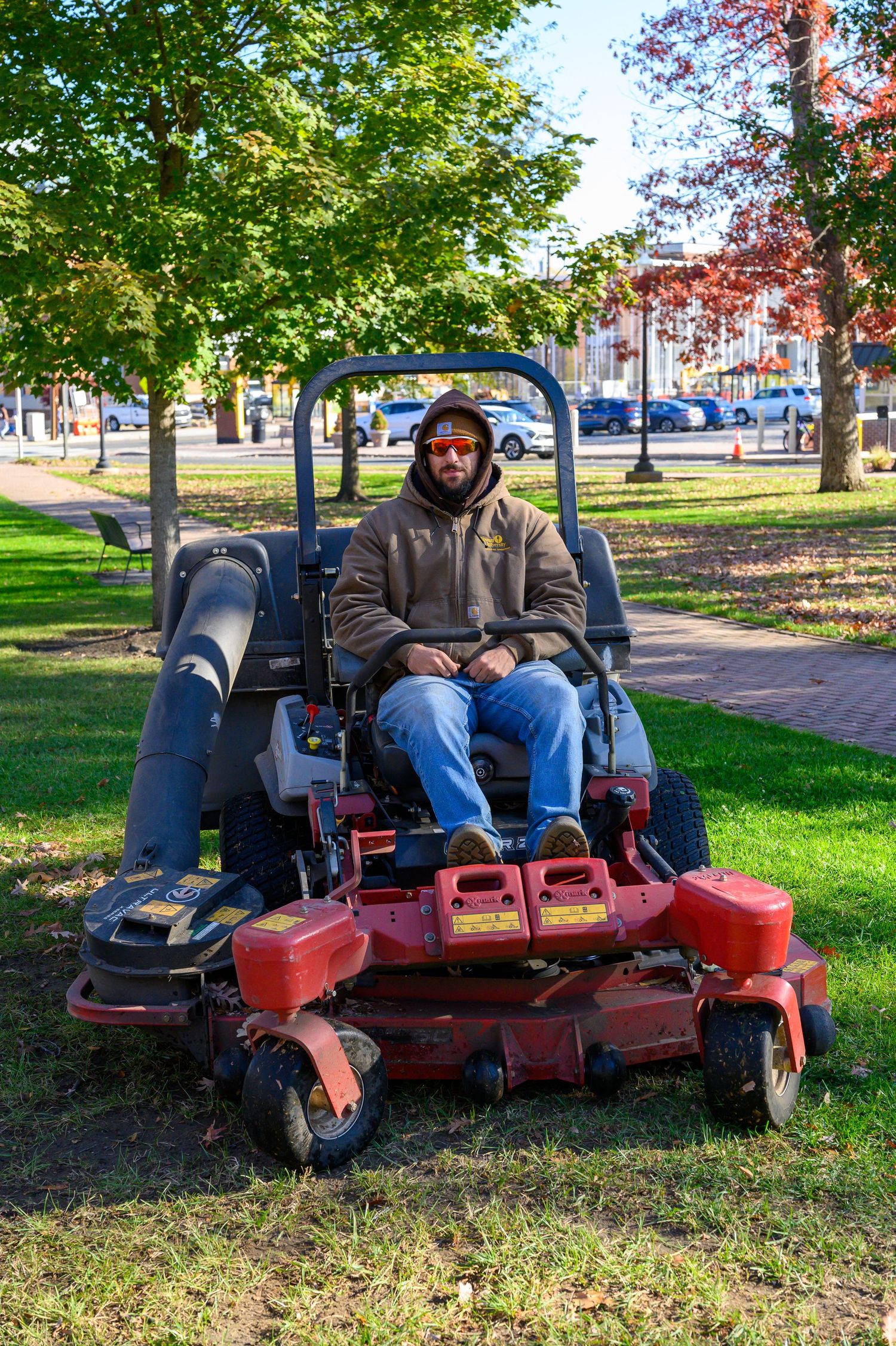 Red commercial lawn mower parked on green grass under autumn trees.