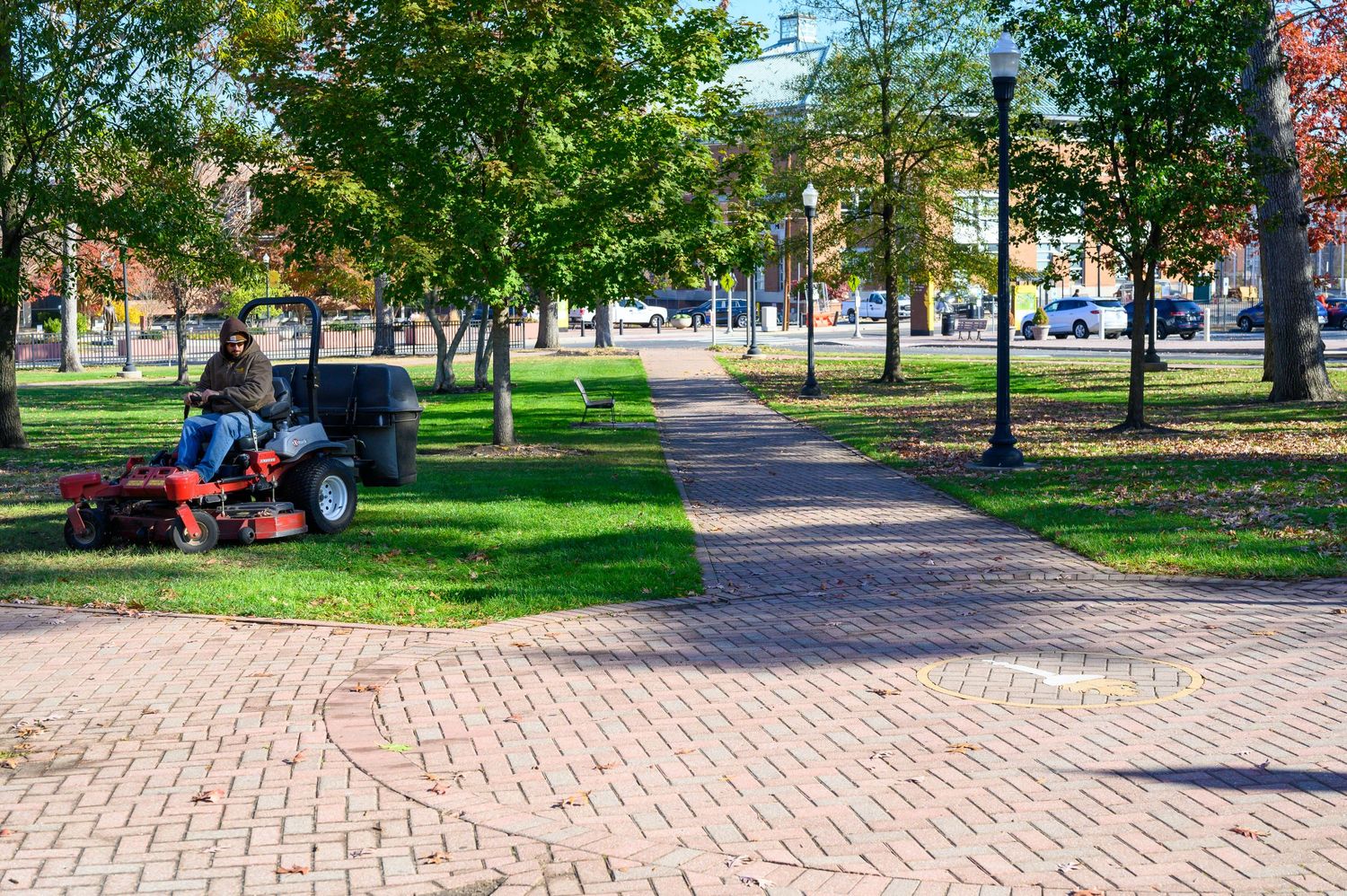 Brick paved walkway through a green park with maintenance equipment visible.