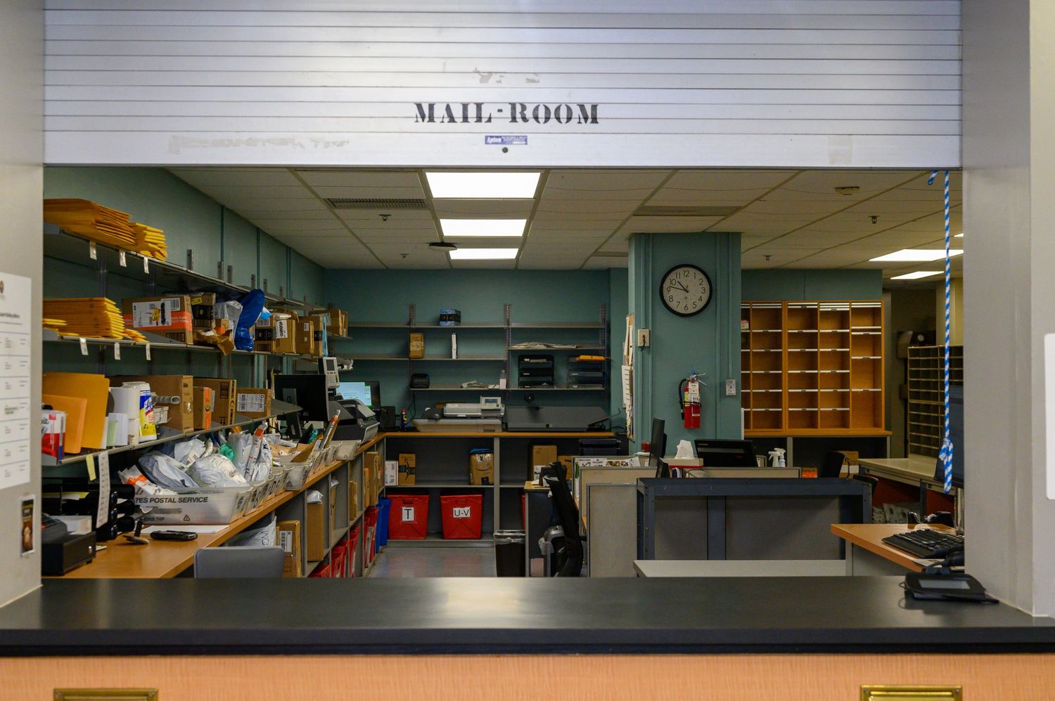 Mail room counter with sorting shelves and fluorescent lighting visible in background.