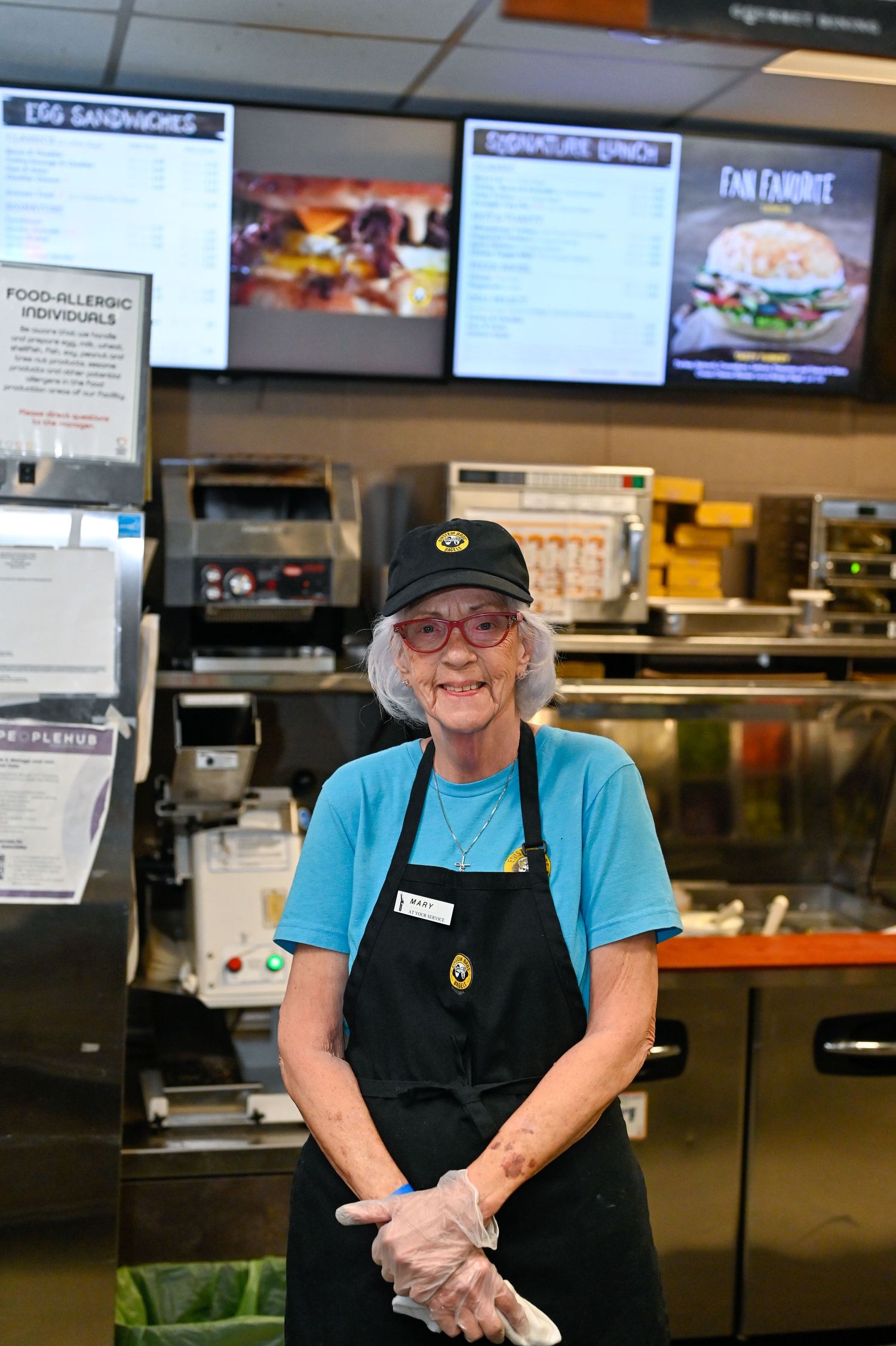 Food service counter with digital menu boards displaying sandwich options.