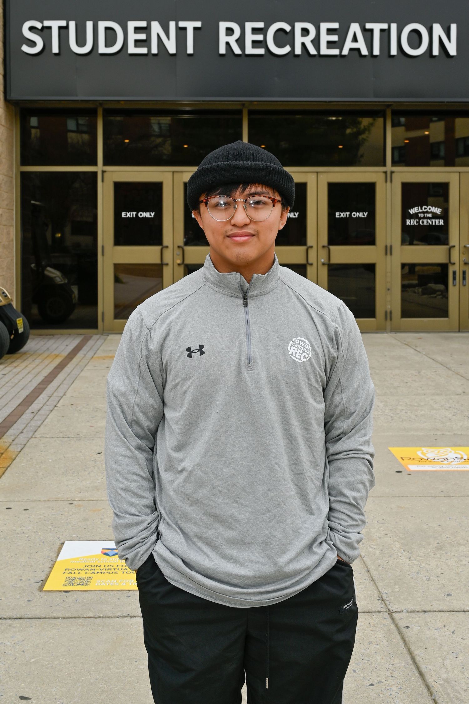 A student wearing an Under Armour quarter-zip stands in front of the Student Recreation entrance.