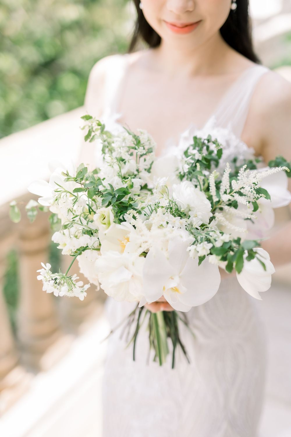 Delicate white floral bouquet with greenery arranged in a romantic garden style against a light background.