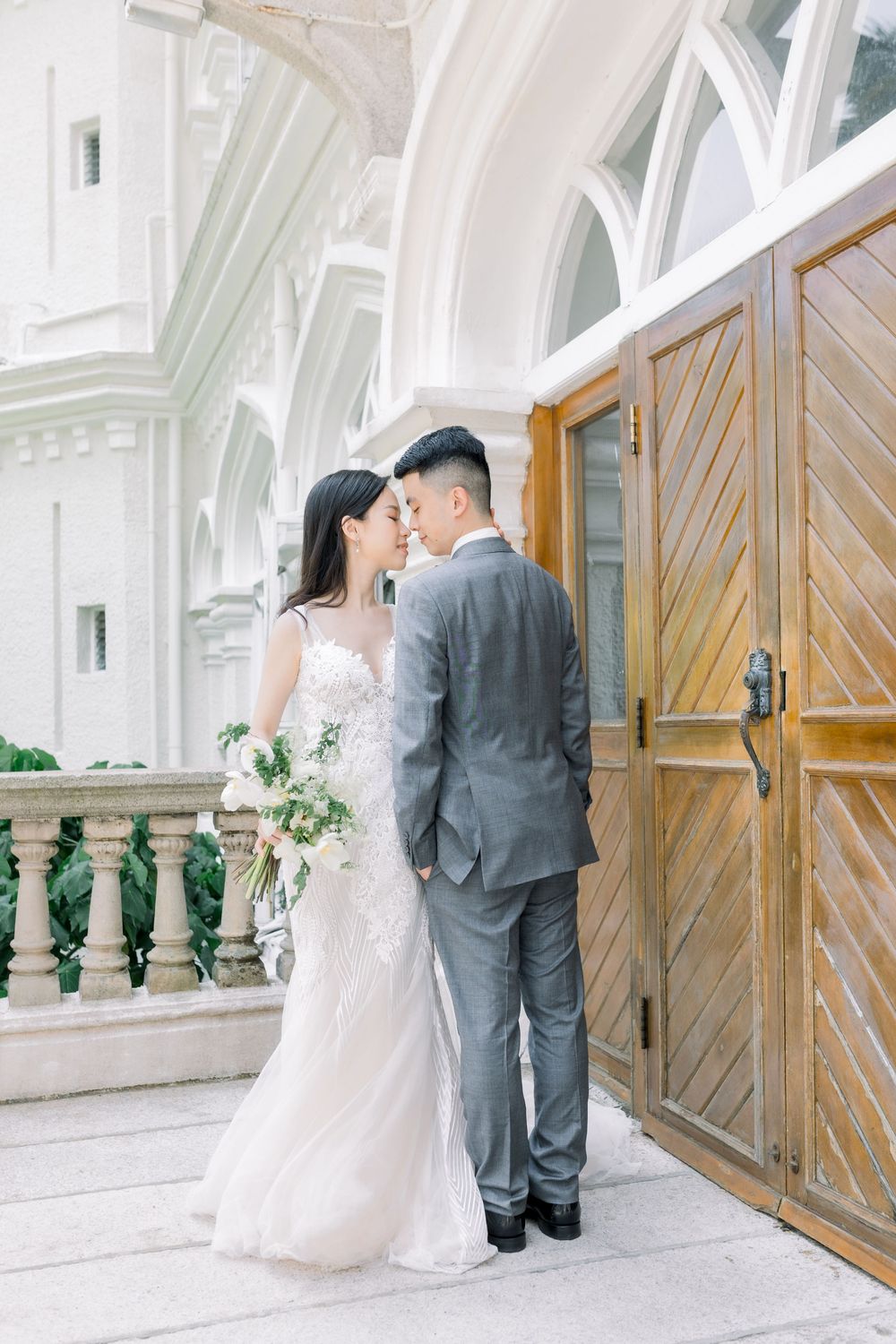 Elegant wedding couple shares intimate moments in front of ornate white church doors with green architectural details.
