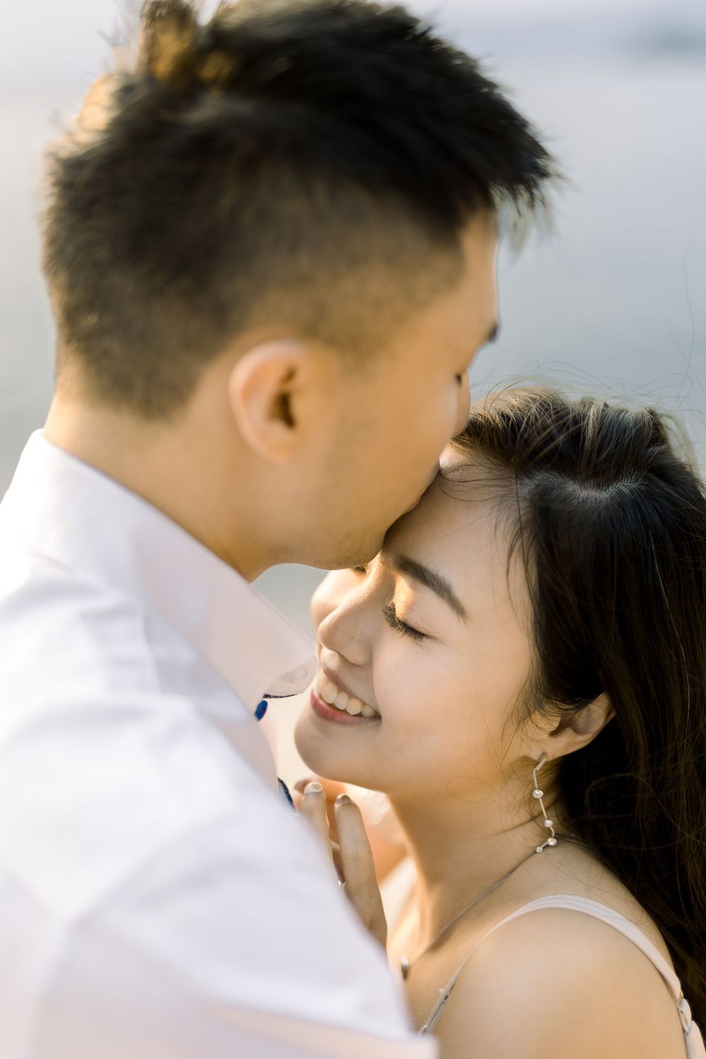 A couple in white clothing share intimate moments in a romantic outdoor photoshoot.