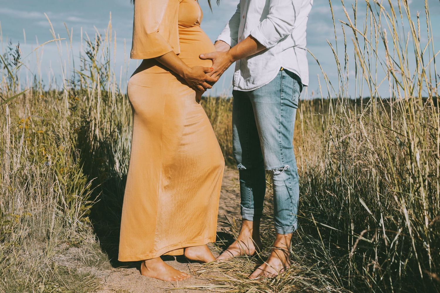 En gravid kvinna och hennes partner står tillsammans i vassen och håller om den gravid magen