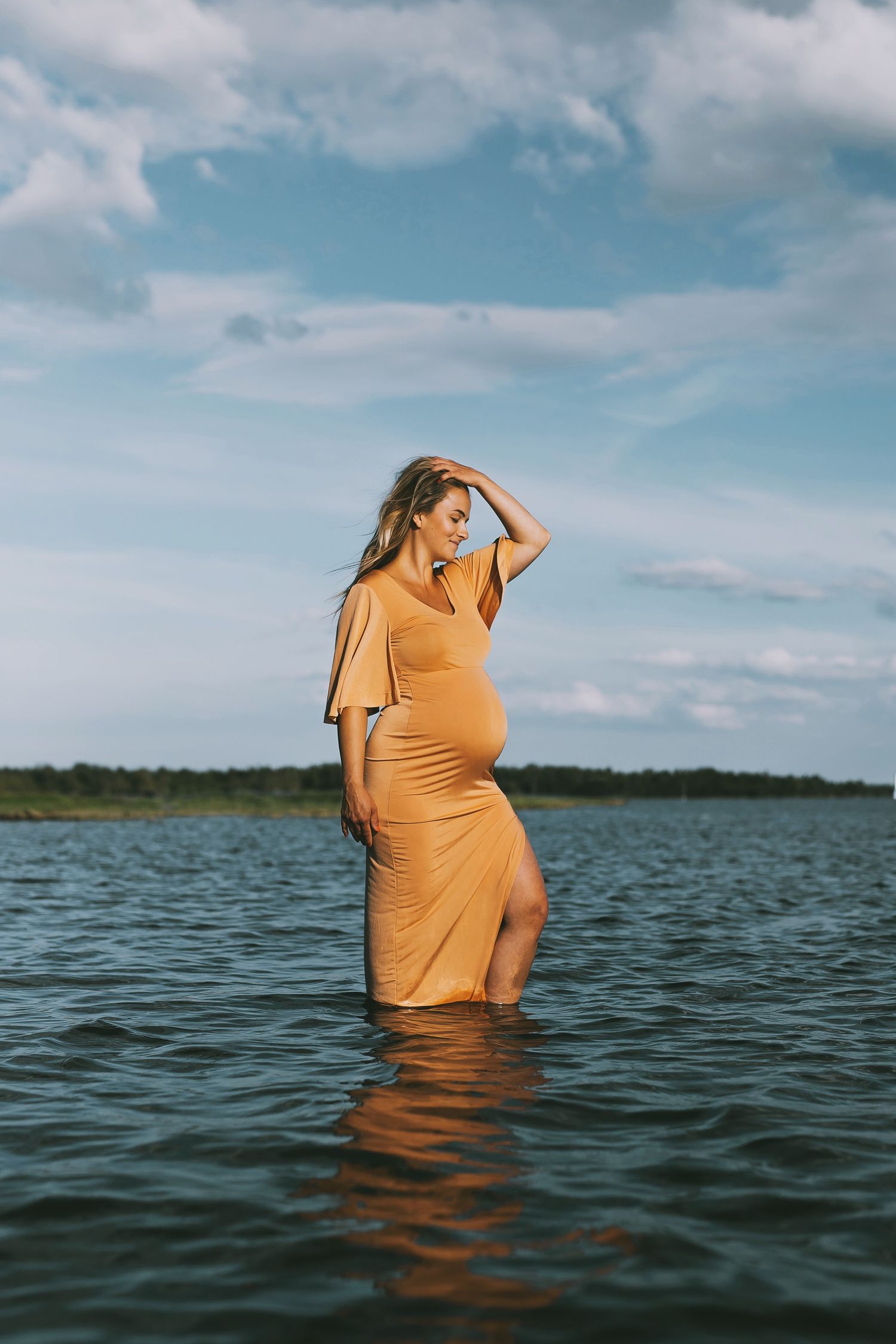 Gravid kvinna med orange klänning som står i havet