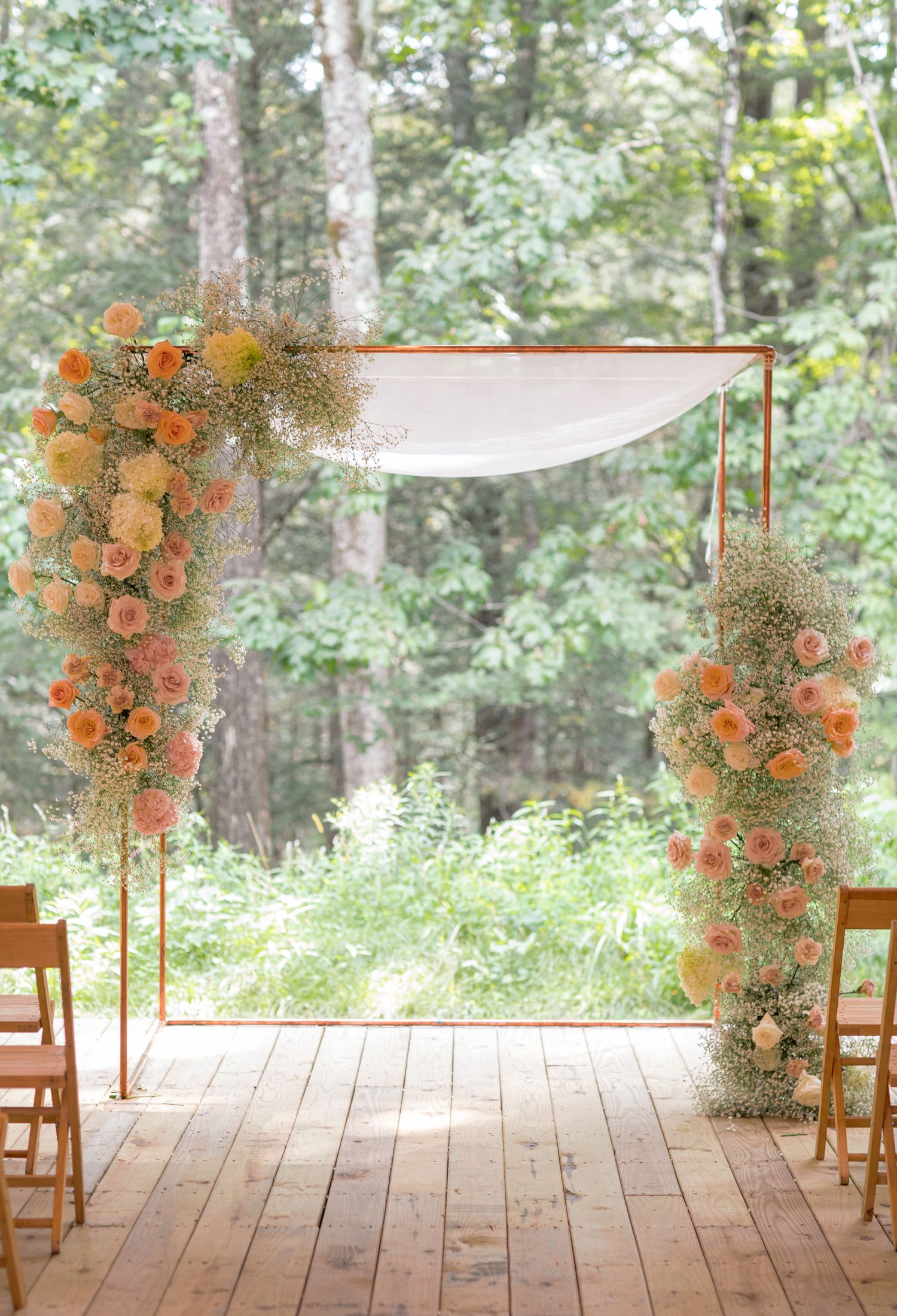 Rustic wooden deck adorned with orange floral arrangements and wooden chairs in a serene forest setting.