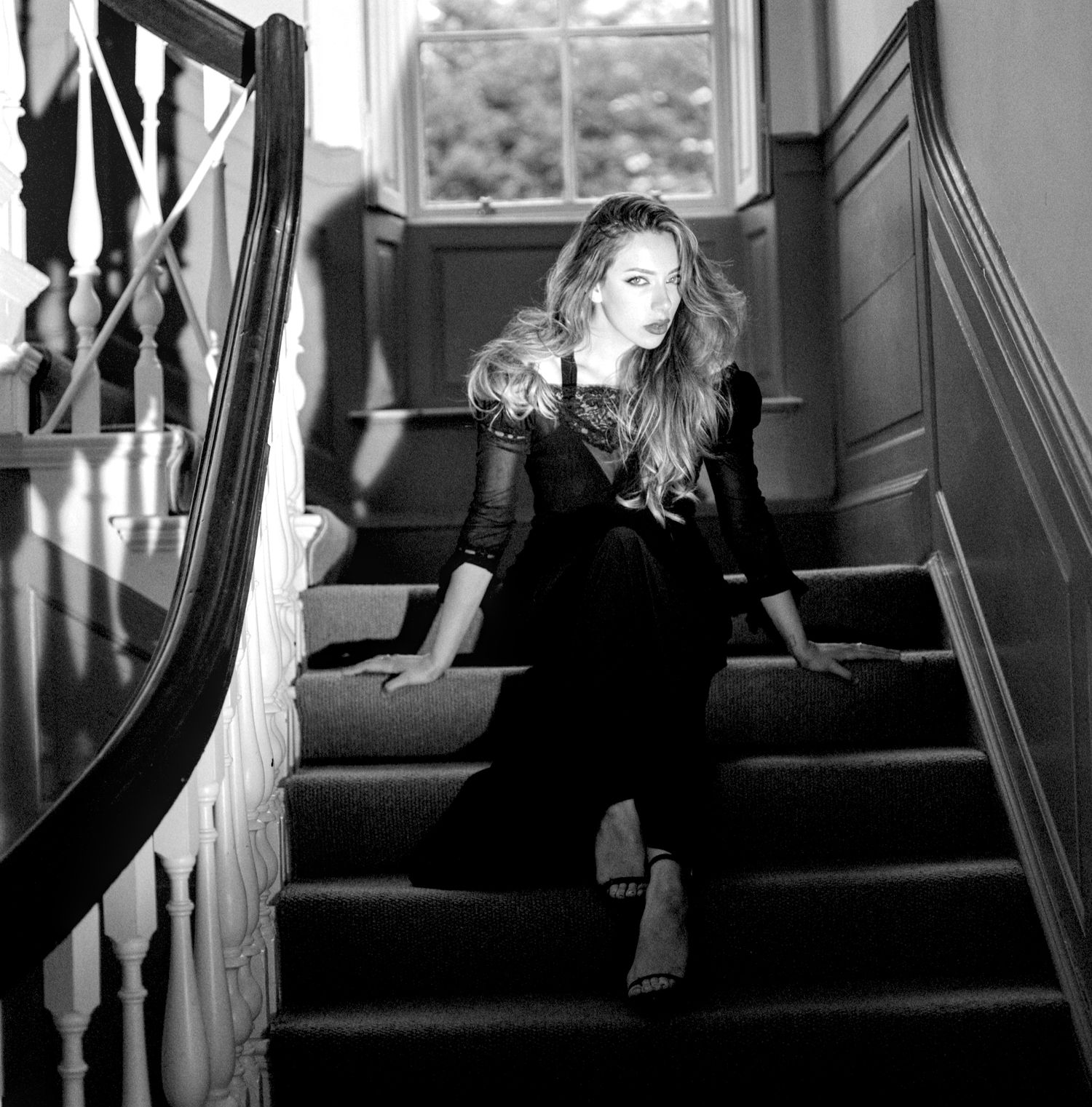 A moody black and white series of photos showing a woman lounging in window seats and on the stairs.