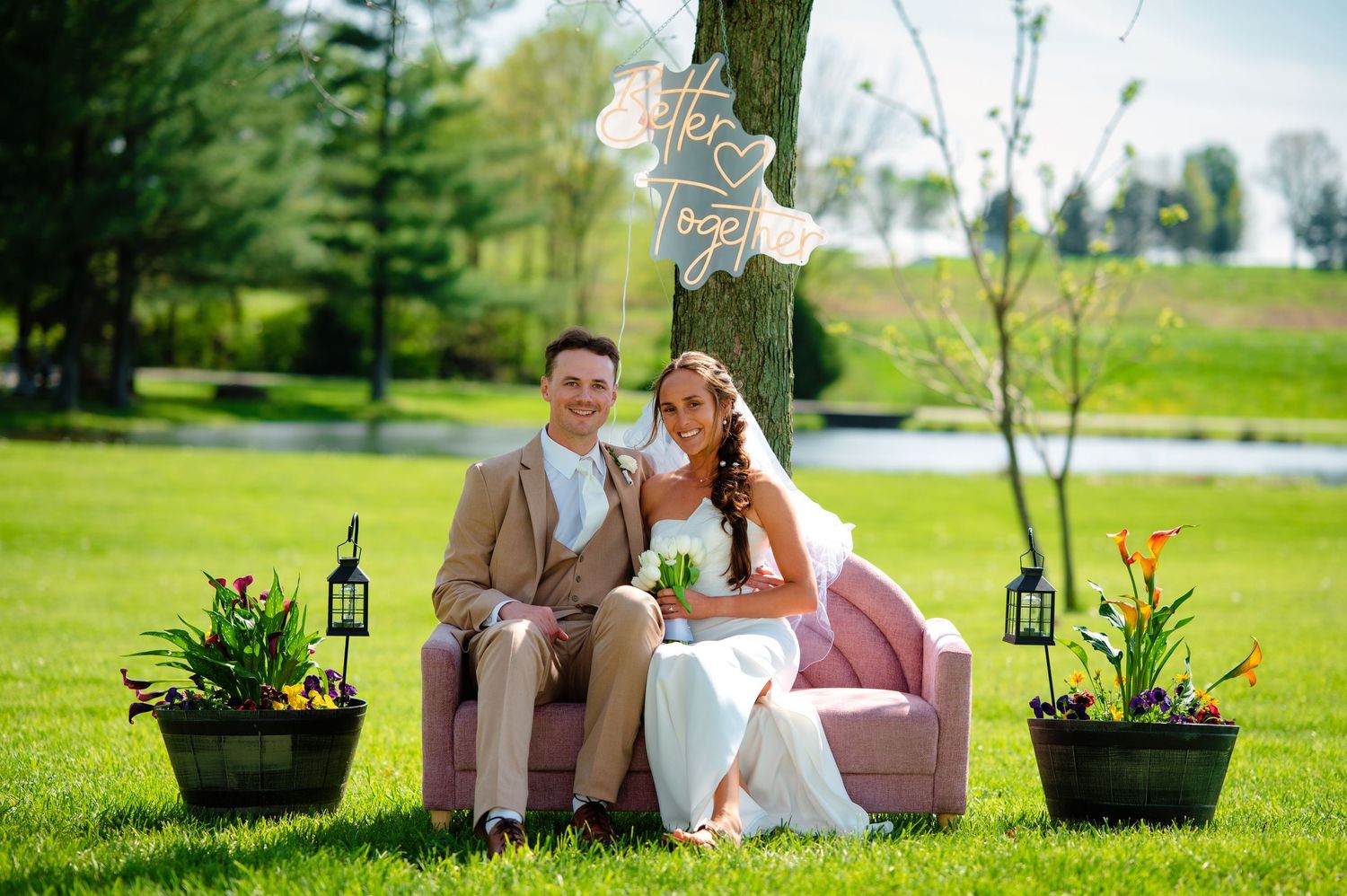 A couple sits on a wooden bench in a lush green garden surrounded by decorative planters and spring flowers.