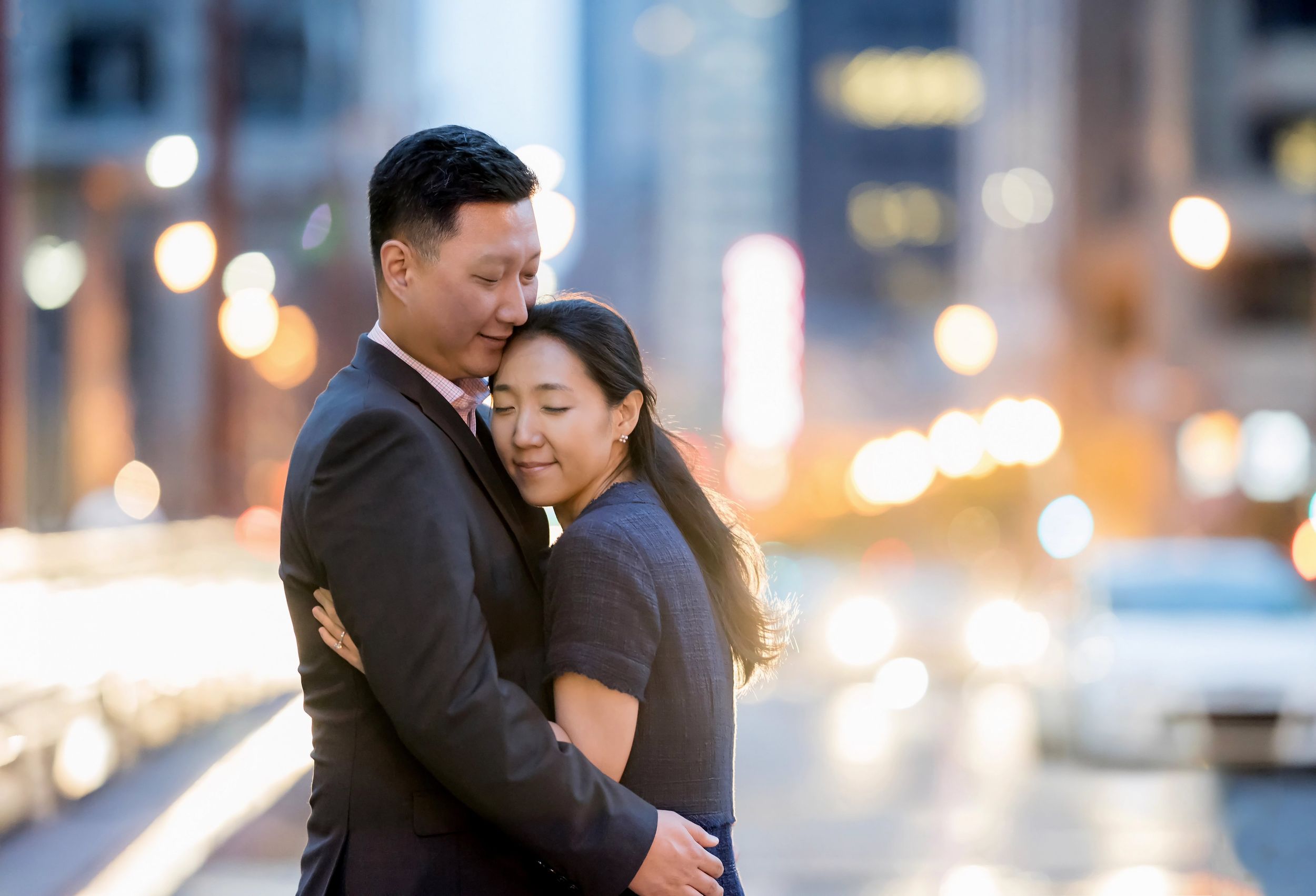 Couple embraces during an evening photoshoot with twinkling city lights in the background.