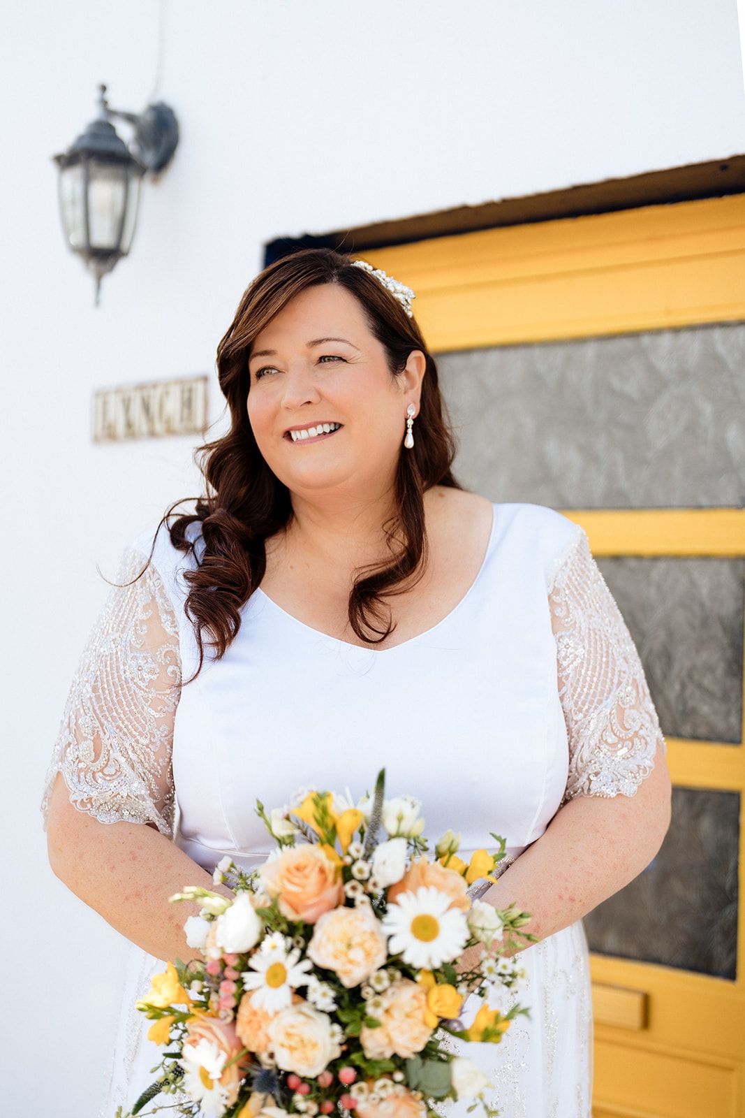 A beautiful spring wedding bouquet featuring peach roses, white daisies and mixed seasonal flowers against a textured background.