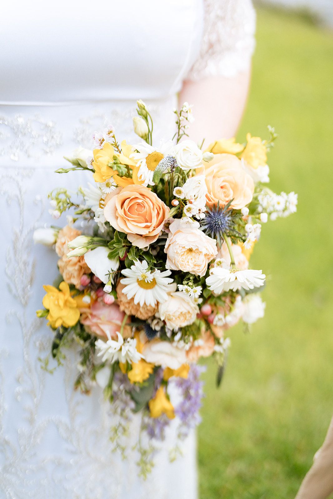 Delicate floral bouquet featuring peach roses, daisies, and wildflowers arranged against a blurred natural background.