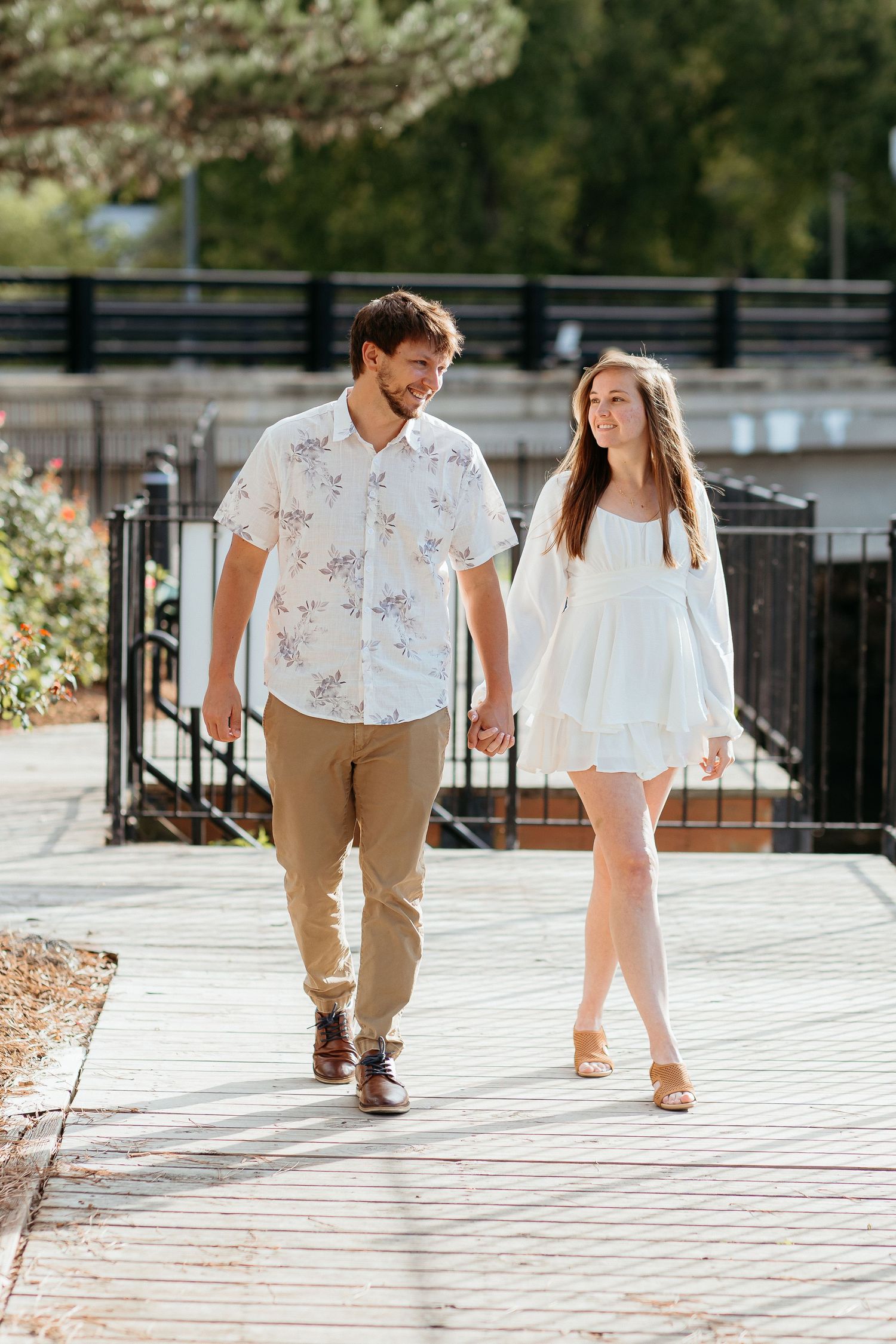 Casual couple walking together on outdoor deck with black railing backdrop. Engagement session, waterfront in Rockford Michigan.
