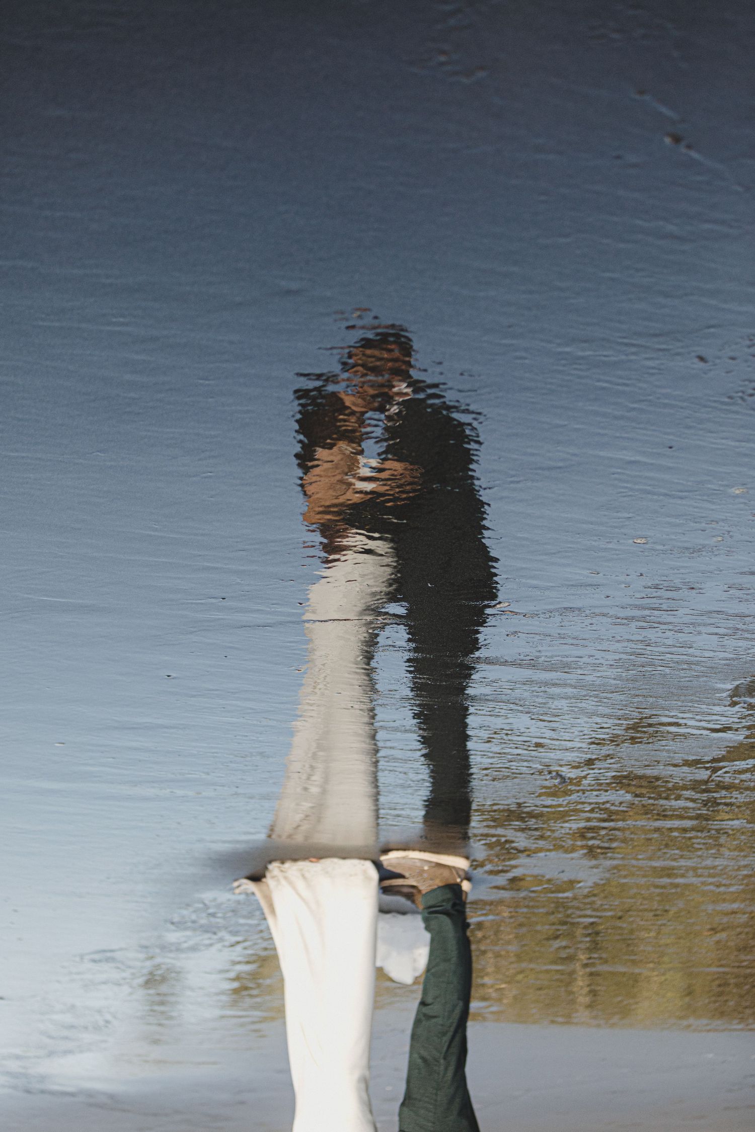 A reflection in water shows two people embracing, creating a mirror-like double image effect on the watery surface.