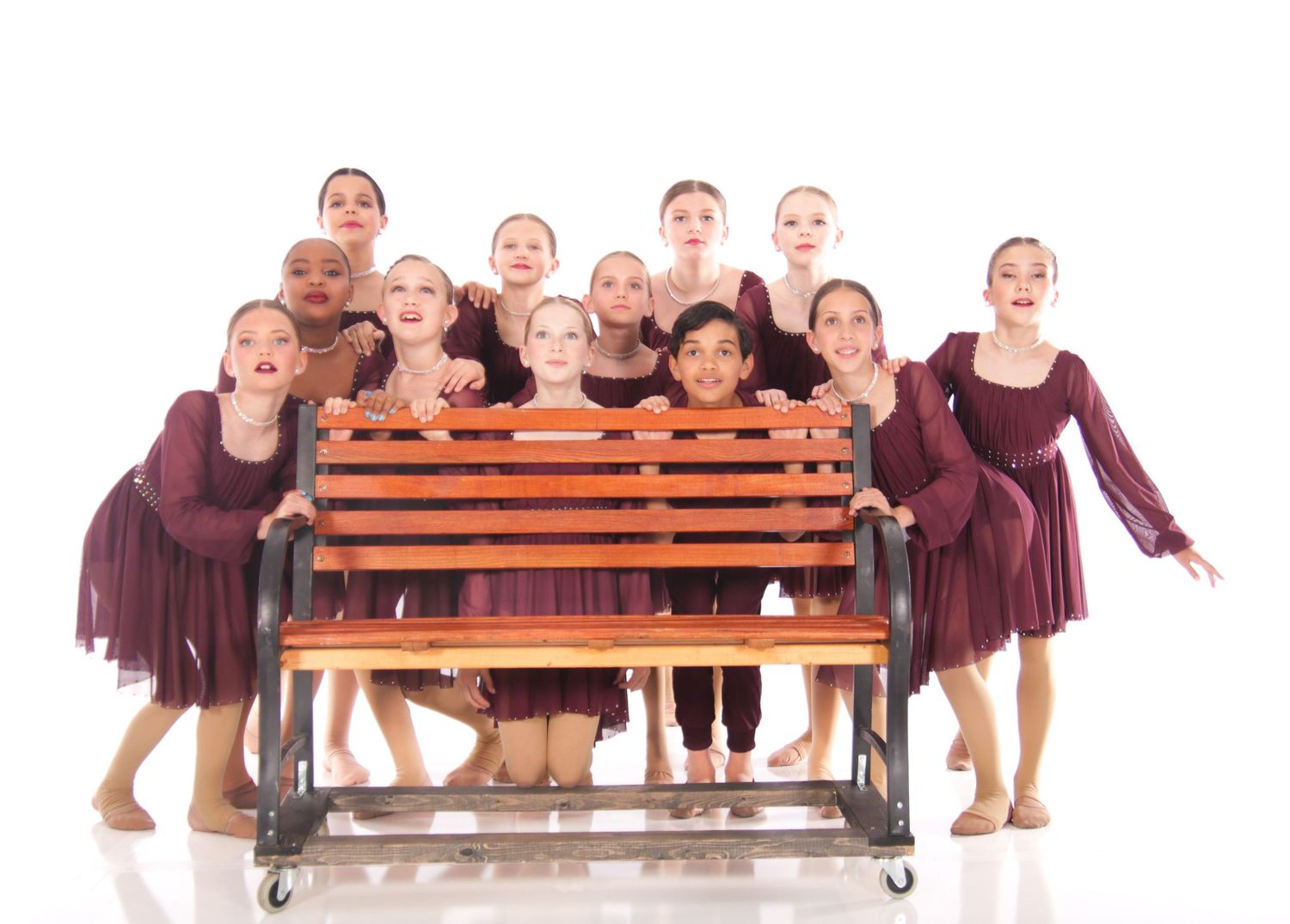 Dance troupe poses on wooden benches in matching burgundy costumes.