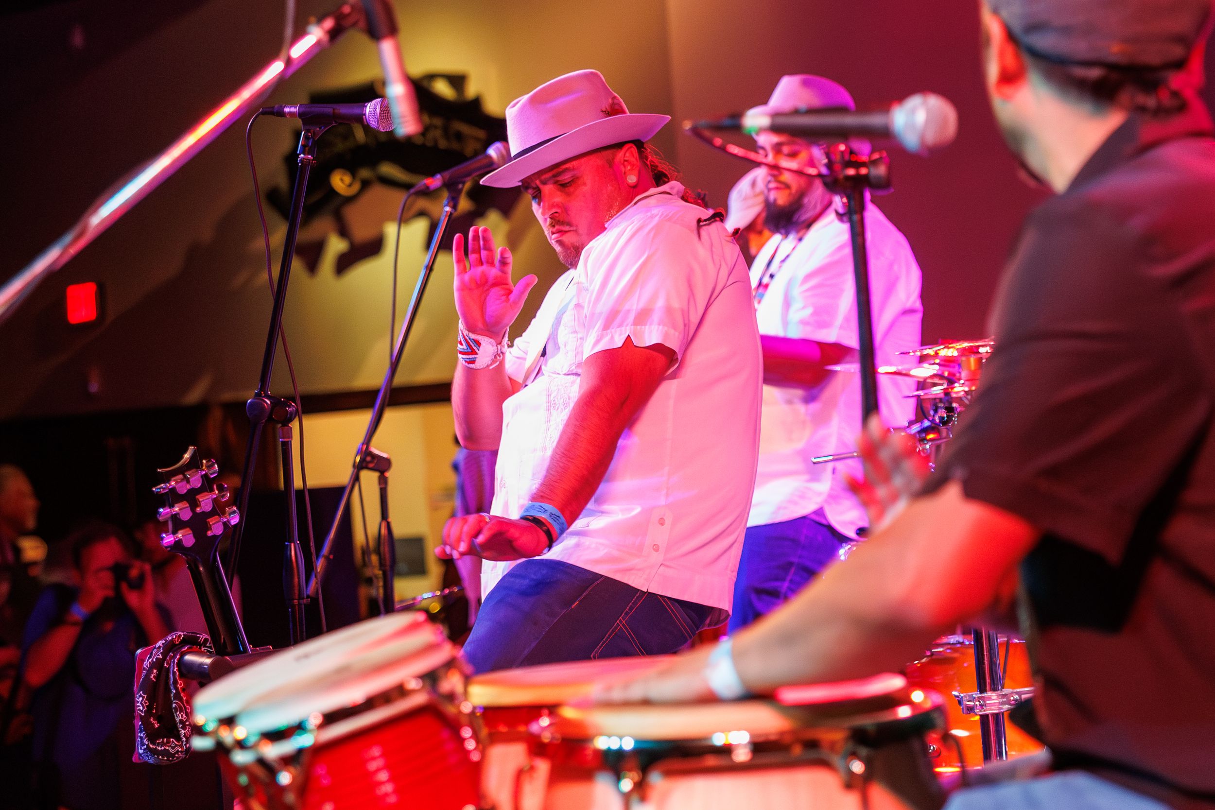 Musicians perform on stage in a dimly lit venue with pink and red lighting creating a vibrant atmosphere.