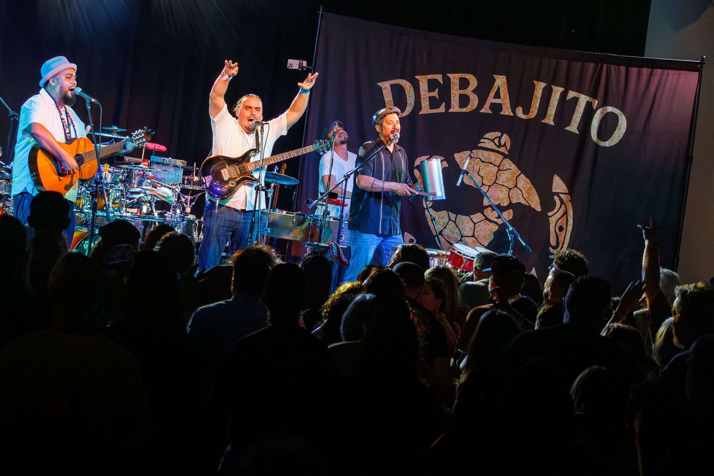 Concert performers on stage with the text 'DEBAJITO' displayed behind them.
