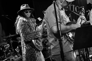 Black and white shot of musicians performing on stage with musical equipment and instruments visible.