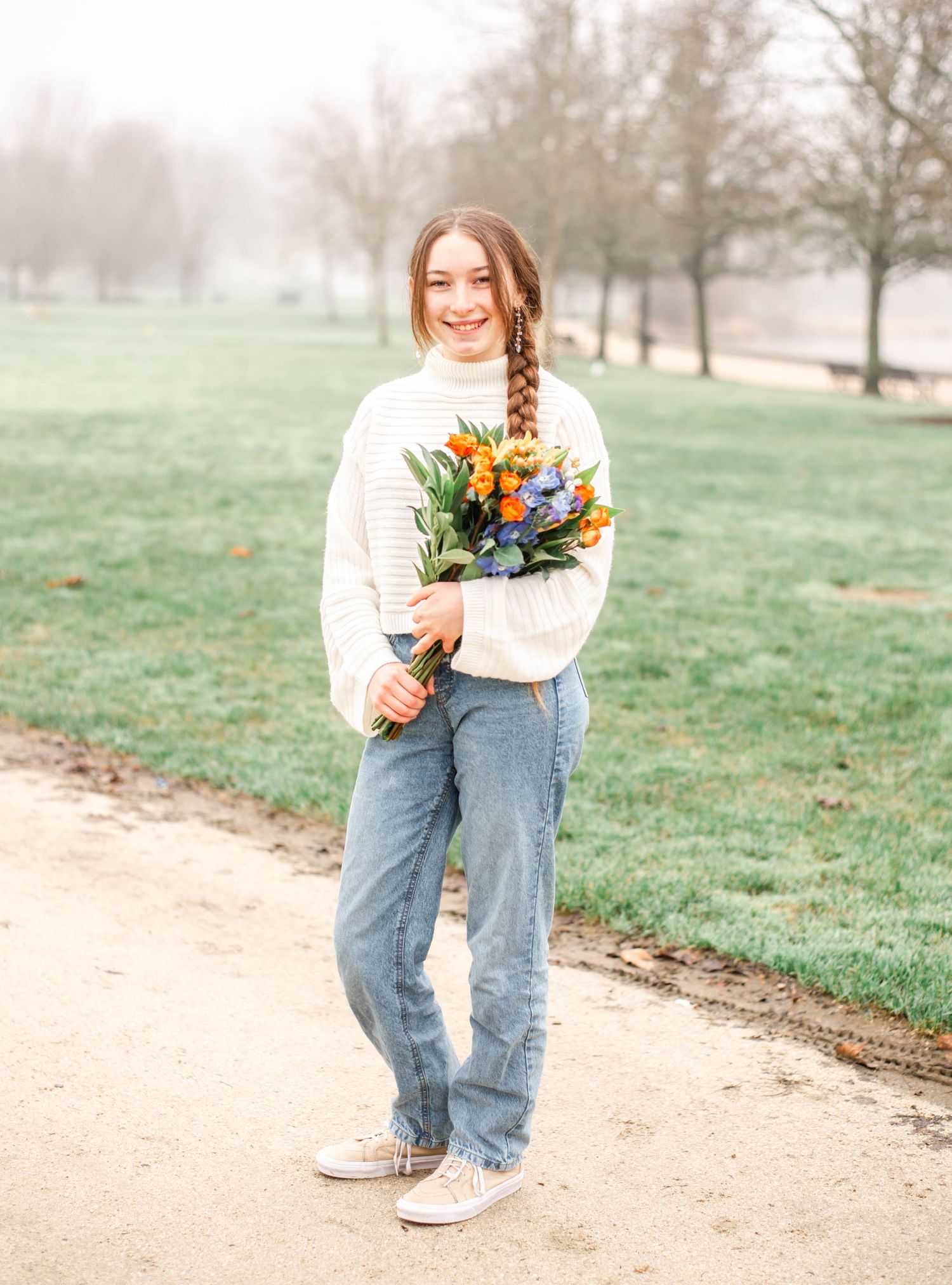 Person in cream sweater holds colorful bouquet featuring orange lilies and purple flowers.