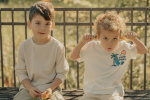 Children in white t-shirts sit around a table outdoors learning and playing together during an educational activity.