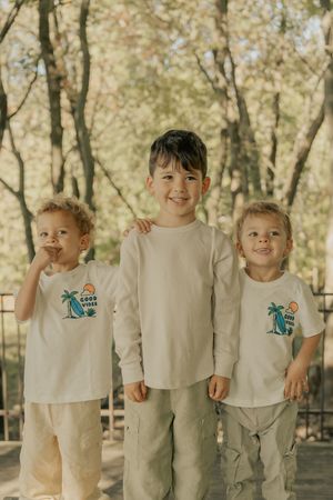 Young children lined up wearing matching beige outfits standing together outdoors in a natural setting.