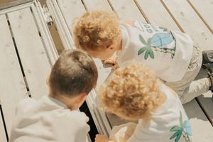 Two children with curly hair lean over a white kitchen counter while mixing ingredients in glass bowls.