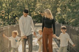 Family walking together holding hands through an autumn park during golden hour with sunlit trees in background.